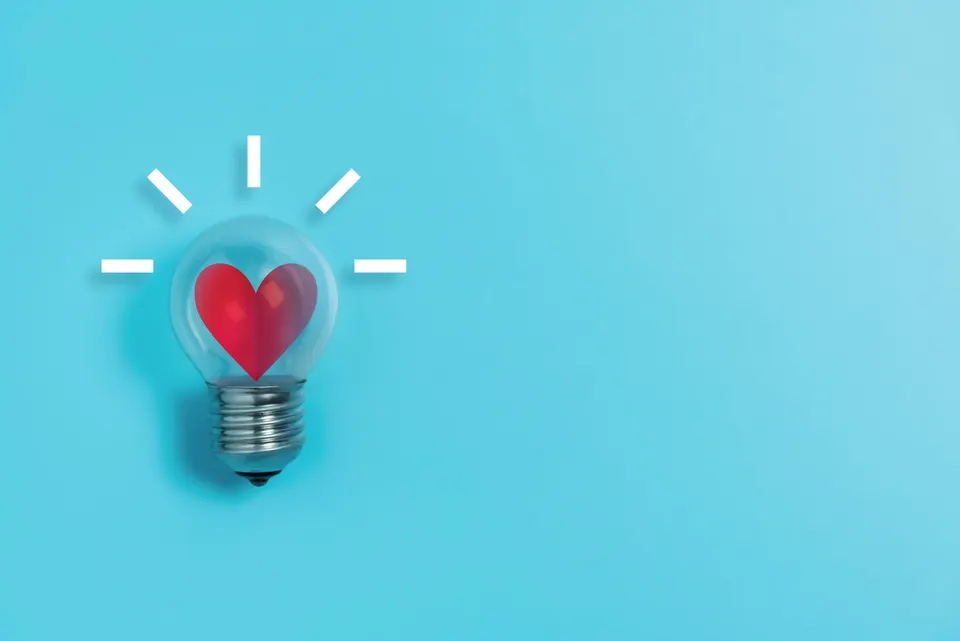 Lightbulb with a red heart inside on a blue background, symbolizing love and ideas.